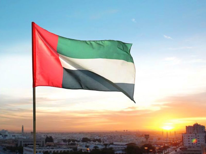 UAE public holidays: UAE flag with sunset of Abu Dhabi and Dubai in the background